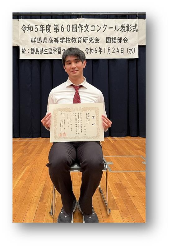 「看板を背景に賞状と田島さんの写真」