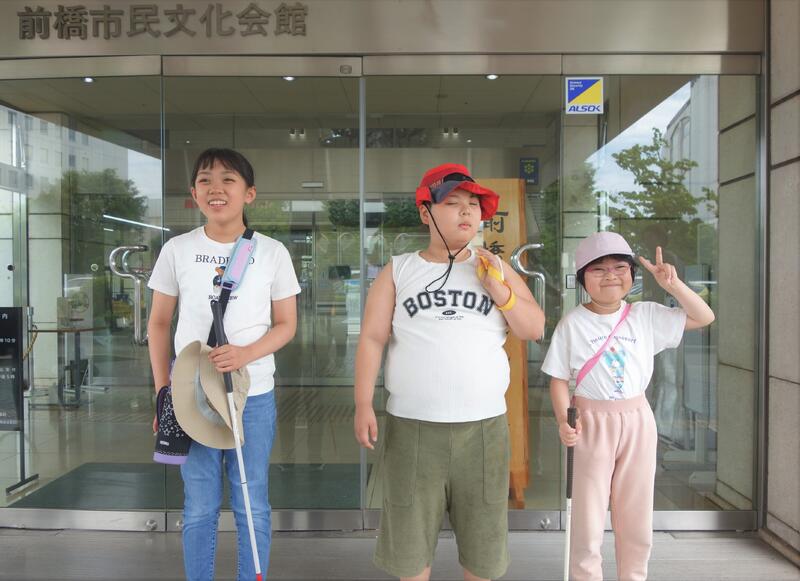 ホールの入り口の前で、３人の児童が並んでいます