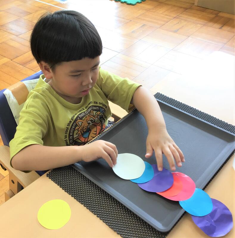 幼児が丸い紙をつなげて貼り、七夕飾りを作っています
