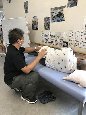 ベッドに寝ている利用者様の腰に、修了生があん摩施術をしている様子