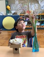 満月のイラストを背景に飾ったすすきを触る幼児