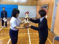 表彰式で先生からトロフィを受け取っている生徒