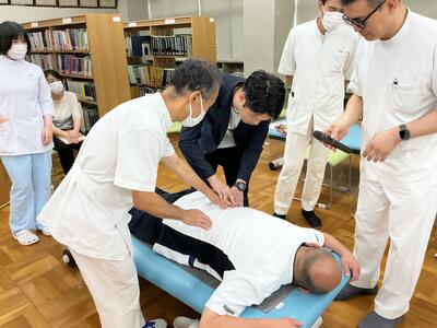職員（手前）の手を取り、状況を解説しながら、丁寧に触診の指導を行う田島先生